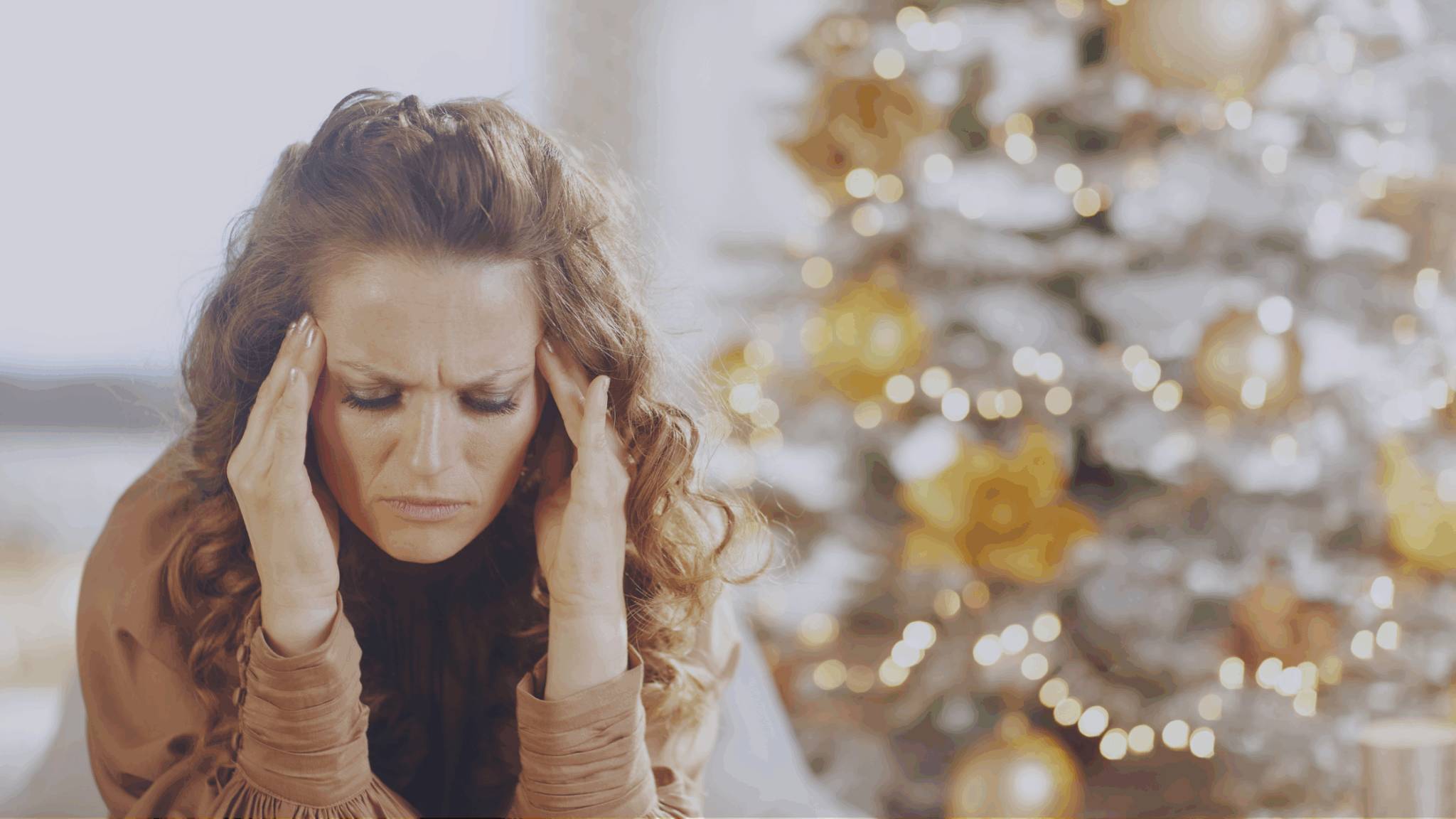 Woman looking tired and frustrated in front of a glowing christmas tree.