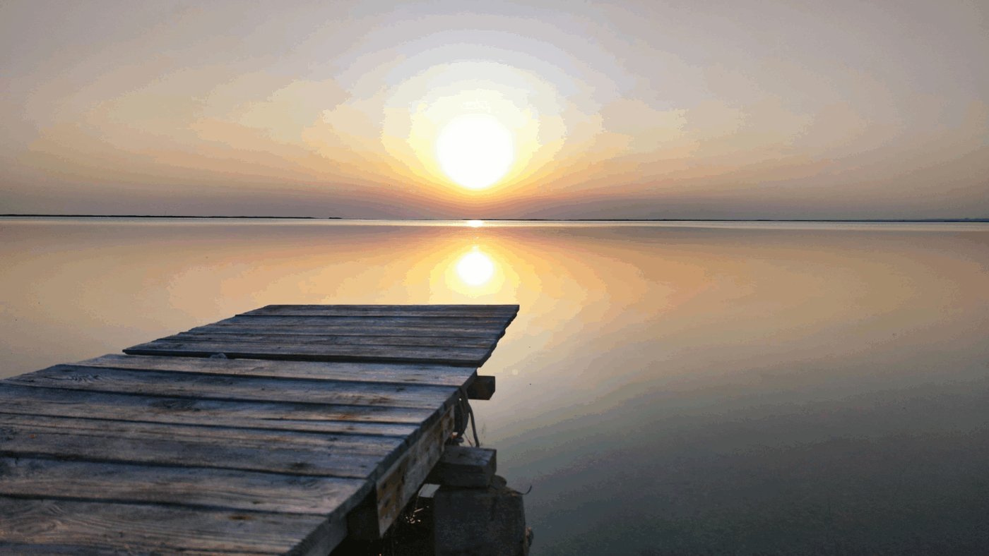 A still lake in the sunset with a wooden jetty.