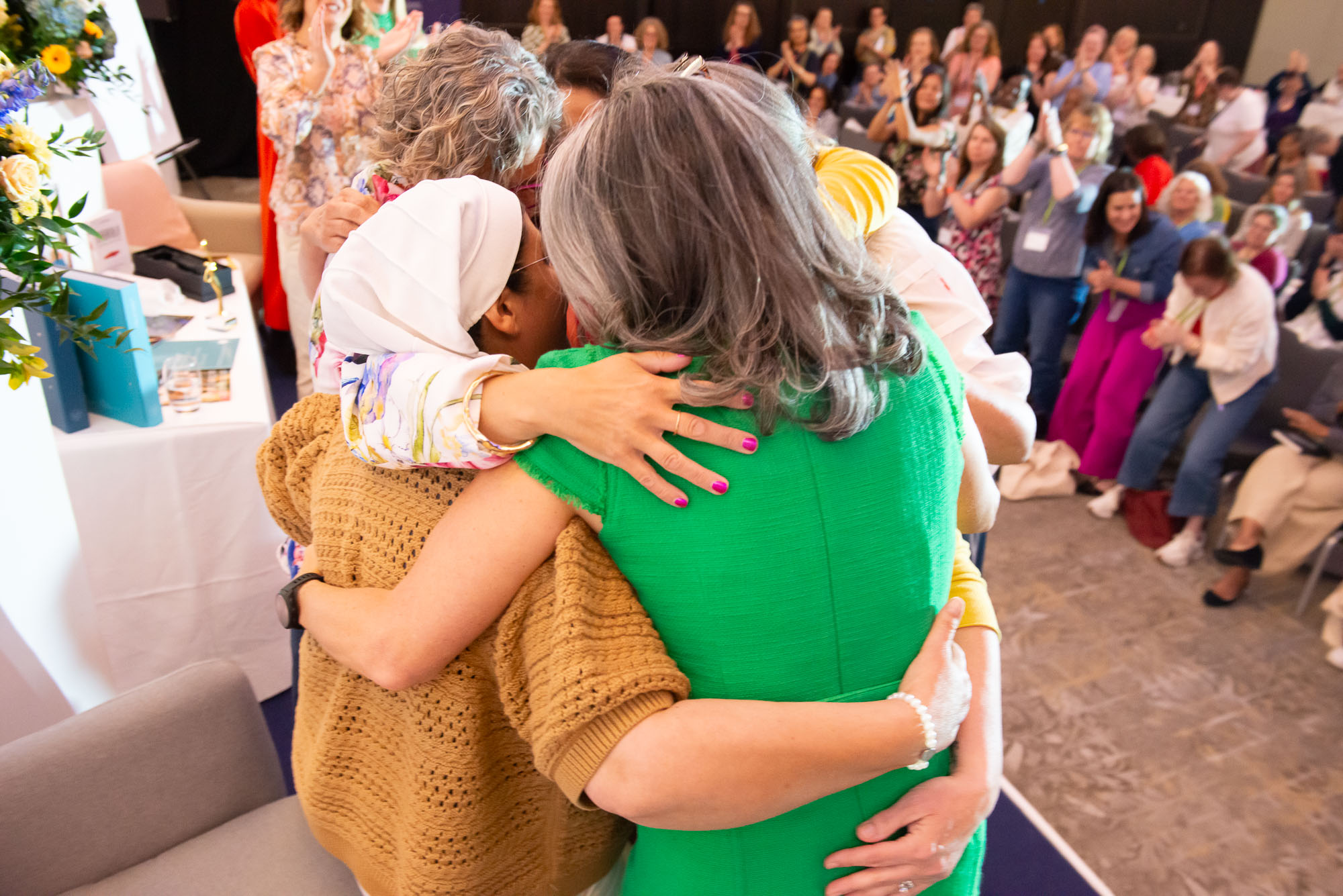 Women hugging on stage at One Woman Conference